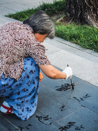 Older woman practicing water calligraphy but due to the heat the Chinese characters disappear immediately and are not readable, Beijing, Chinaのeditorial素材