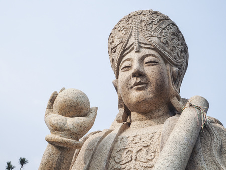 Qingdao, China - December 2017: white carved buddhist sculpture holding a ball and scroll at the entrance to Yanku scenic area at Mt. Laoshanのeditorial素材