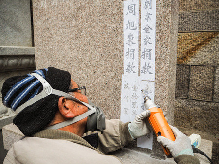 Qingdao, China - December 2017: Older man carving names and donation amount on s stele in Taiqing temple, Laoshanのeditorial素材