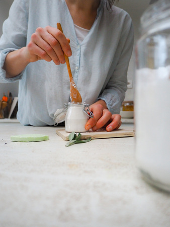 Caucasian woman making homemade vegan deodorant in a glass jar adhering to a zero waste and plastic...