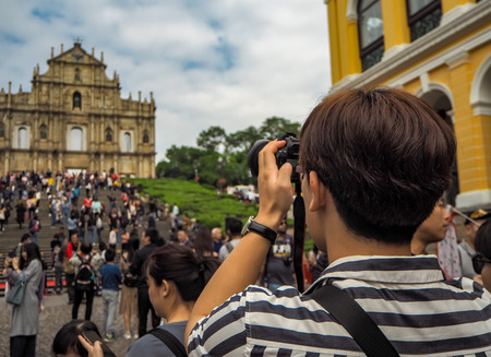 November 2018 - Macao, China: Young Asian man using a camera to take a picture of the Ruins of St. Paul's in a large mass of Chinese touristsのeditorial素材
