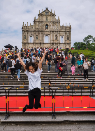 November 2018 - Macao, China: Young Asian woman posing for a jumping picture in front of the ruins of St. Paul's in a large mass of Chinese touristsのeditorial素材