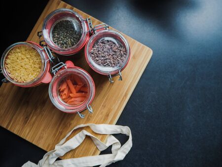 Four glass jars filled with dry food ingredients such as gluten free red lentil pasta and black...
