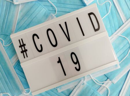 Blue surgical face masks with a white light box stating # Covid-19の写真素材