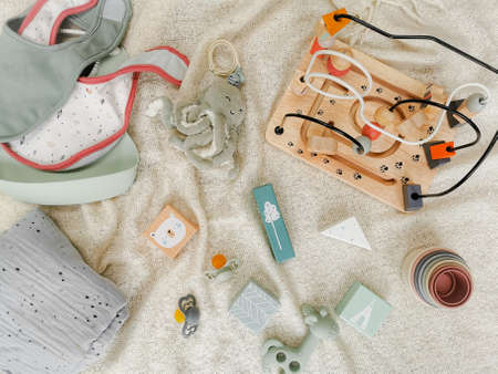 Gender neutral toys for babies in muted soft colors. Wooden blocks and bead frame, teething toy, bib, bead. Flat lay. Gender neutral parenting.の写真素材