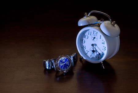 A traditional alarm clock and a wrist watch on a dark brown background