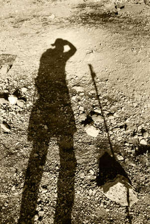 The shadow of a trekker taking a photo and his trekking pole on the scree and gravel - the barren terrain of Mt Kilimanjaro, Tanzania - in monochromeの写真素材