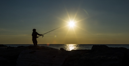 Man fishing in the first rays of sunlight on sea shoreの写真素材