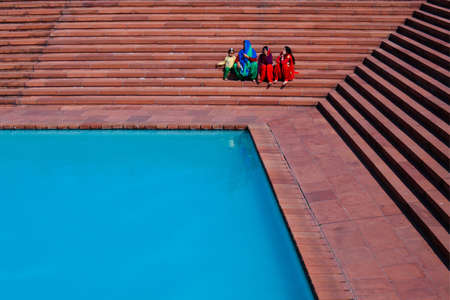 02/05/2015. India, Dehli. Four ladies in national clothes sitting on the stairs near the poolのeditorial素材