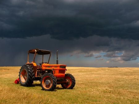 a farm tractor in a field against storm cloudsの写真素材