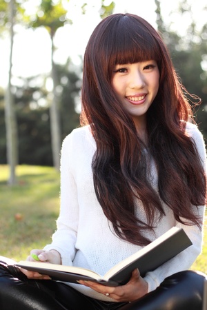 A smiling Asian student is studying at the park.の写真素材