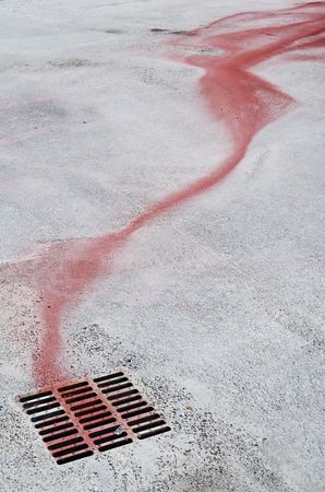 Red ink flow running down to a manhole coverの写真素材