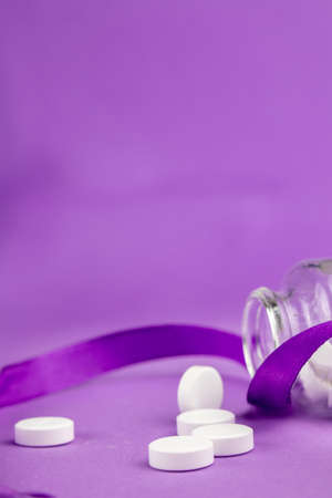 White pills in a jar with purple ribbon on a purple background.の写真素材