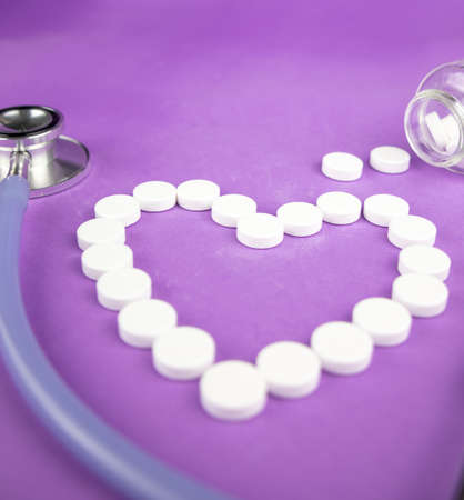 Heart made of white pills on a purple background with stethoscope.の写真素材