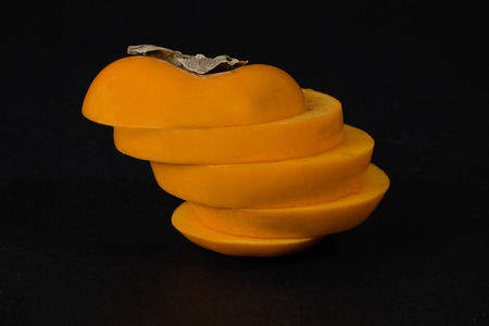 Persimmon fruit with slices on a black background