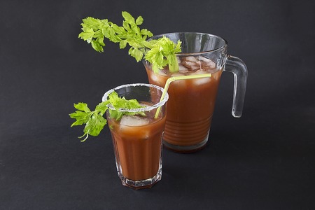 a glass with a cocktail "Bloody Merry" with ice and a sprig of celery on a black background, the top of the glass is decorated with saltの写真素材