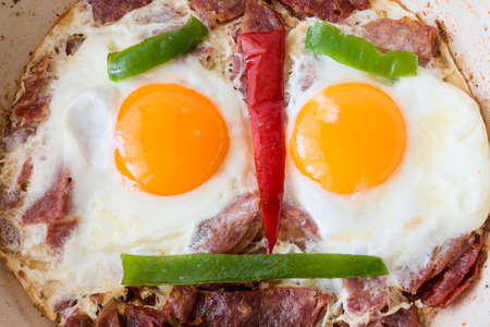 Smiling happy face frying eggs breakfast with bacon and peppers in a panの写真素材