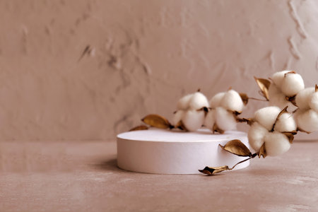 white round podium with branch of cotton on beige natural background. Mockup to promote eco or organic product , cosmetics.の写真素材