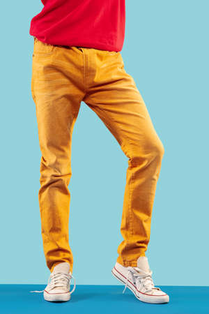 Young fashion mans legs in brown trousers and white sport shoes on blue floorの写真素材