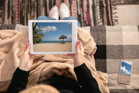 Young beautiful girl sitting at home on sofa choosing next trip online.の写真素材