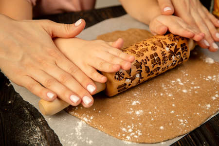 Close-up child and female hands making festive cookies with rolling-pin.