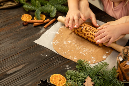 Close-up child and female hands making festive cookies with rolling-pin.