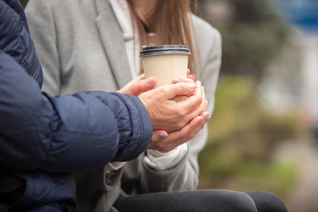 Close-up old female hands with cup of coffee. Autumn family walk.の写真素材