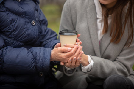Close-up old female hands with cup of coffee. Autumn family walk.の写真素材