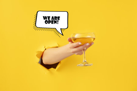 Female hand with cocktail glass torn through yellow paper background.の写真素材