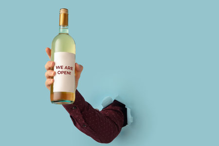 Mans hand holding bottle of wine and torn through blue paper background.の写真素材