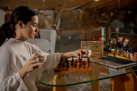 Young beautiful girl sitting at home and playing chess with friend online.の写真素材