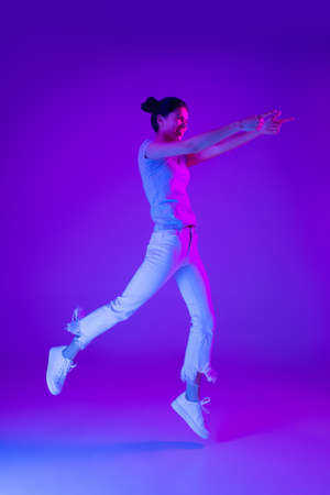 Young beautiful girl jumping isolated on multicolored background in neon light.