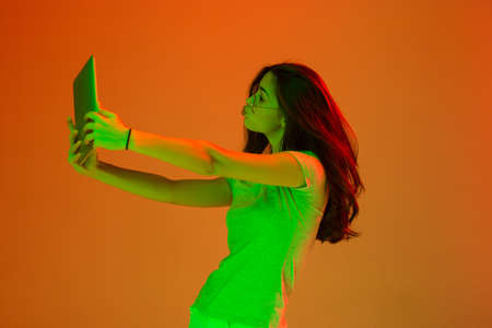 Happy girl with digital tablet isolated on studio background in neon light.の写真素材