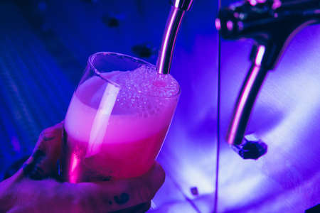 Close-up beer glass in barman hand in multicilored neon light.の写真素材