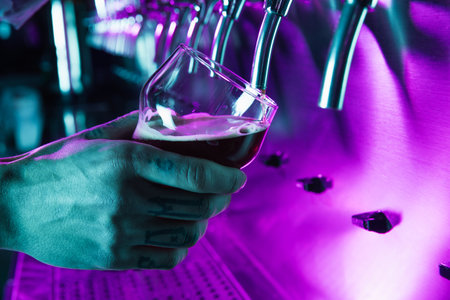 Close-up male hand with glass pouring beer from tap to glass in neon light.の写真素材
