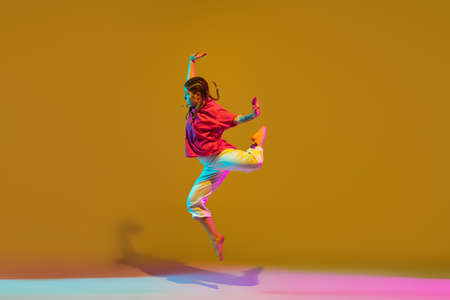 Sportive girl dancing hip-hop in attire on colorful background in neon lightの写真素材