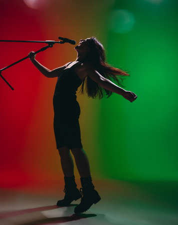 Portrait of young female singer isolated on green-red background.の写真素材