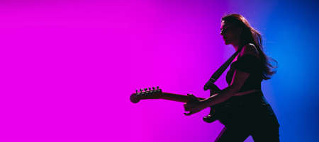 Silhouette of young female guitarist isolated on gradient background in neon.