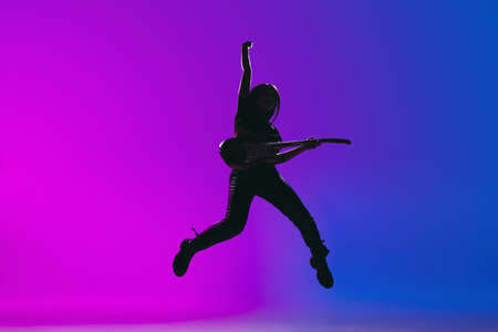 Silhouette of young female guitarist isolated on gradient background in neon.