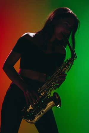 Silhouette of young girl with saxophone posing isolated on green-red background.の写真素材