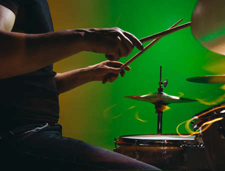 Close-up of male hands playing drums isolated on green-red background in neonの写真素材