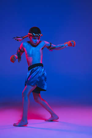 Young boy thai boxer training over blue background in neon light.