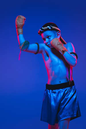 Portrait of little boy thai boxer posing over blue background in neon light.の写真素材