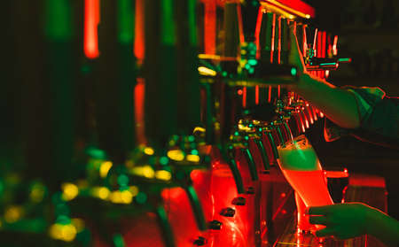 Close-up beer pumps taps in pub or bar in multicolored neon light.の写真素材