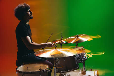 Portrait of young man drummer playing isolated on green-red background in neonの写真素材