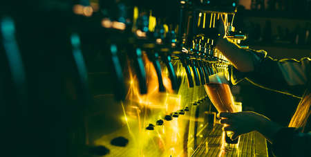 Young woman barman pouring a cold lager beer from tap to glass in neon light.の写真素材