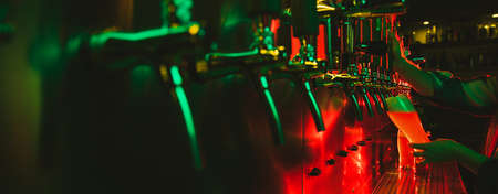 Close-up beer pumps taps in pub or bar in multicolored neon light.の写真素材