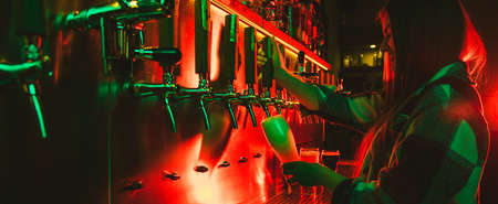 Young woman barman pouring a cold lager beer from tap to glass in neon light.の写真素材