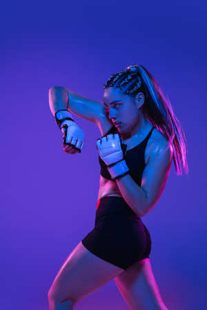 Athletic female MMA fighter training over blue-pink background in neon lightの写真素材