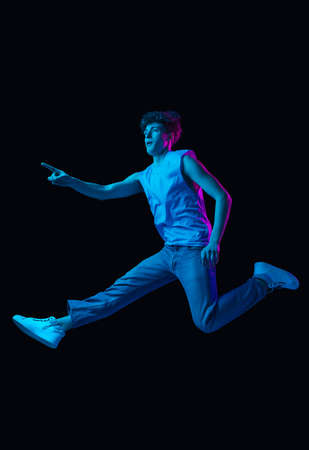 Young happy Caucasian man jumping isolated on dark background in neon light
